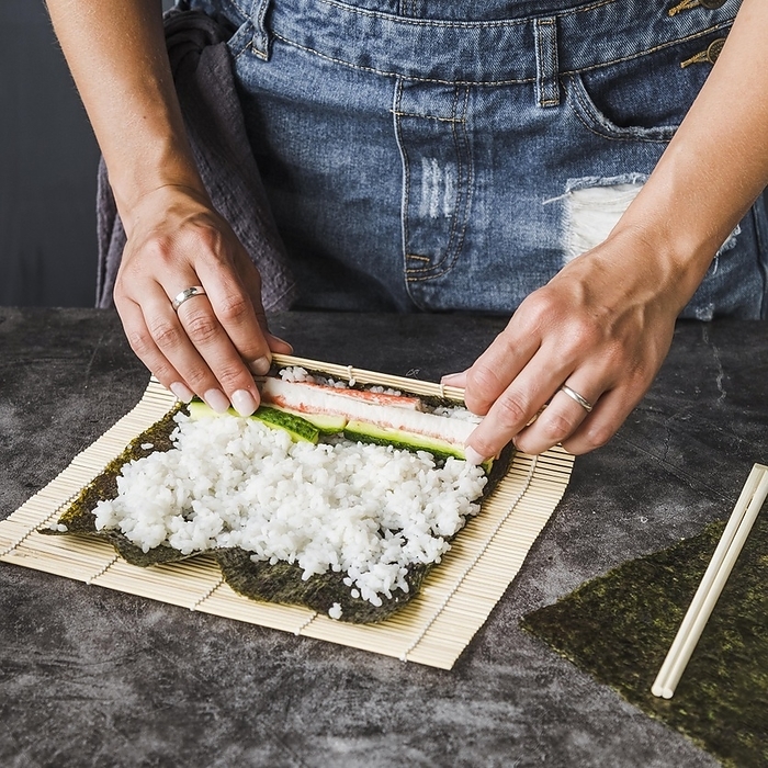 Hands wrapping ingredients sushi mat, by Oleksandr Latkun