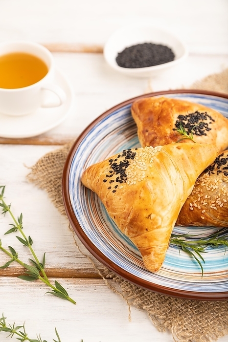 Homemade asian pastry samosa, cup of green tea on white wooden background and linen textile. side view, selective focus, by ULADZIMIR ZGURSKI