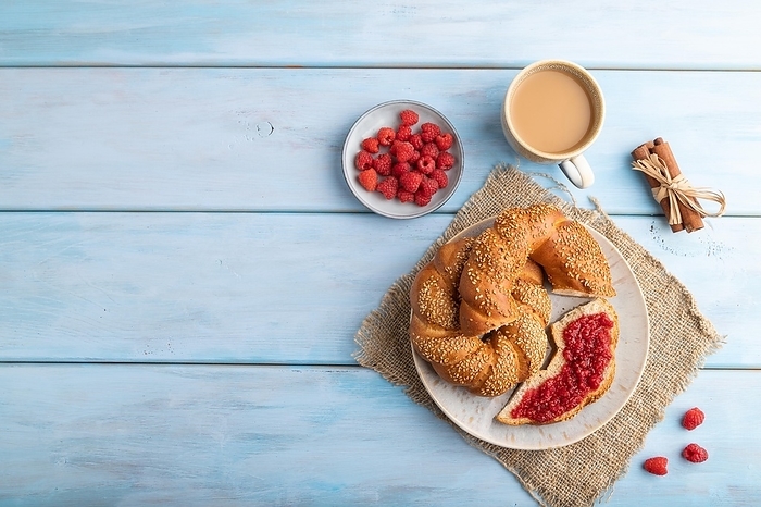 Homemade sweet bun with raspberry jam and cup of coffee on a blue wooden background and linen textile. top view, flat lay, copy space, by ULADZIMIR ZGURSKI