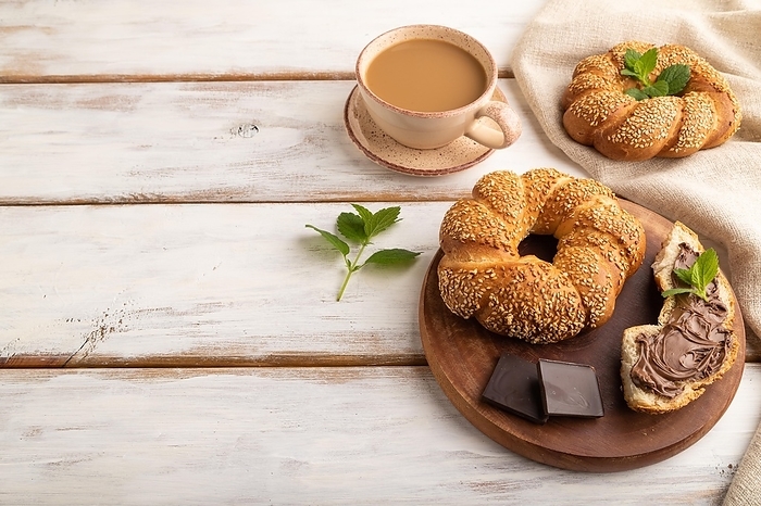 Homemade sweet bun with chocolate cream and cup of coffee on a white wooden background and linen textile. side view, copy space, by ULADZIMIR ZGURSKI