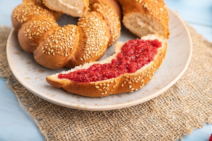 Homemade sweet bun with raspberry jam and cup of coffee on a blue wooden background and linen textile. side view, close up, selective focus, by ULADZIMIR ZGURSKI