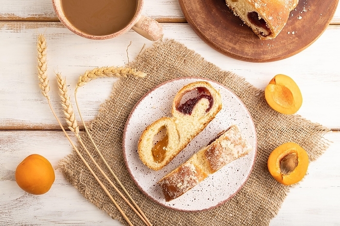 Homemade sweet bun with apricot jam and cup of coffee on white wooden background and linen textile. top view, flat lay, close up, by ULADZIMIR ZGURSKI