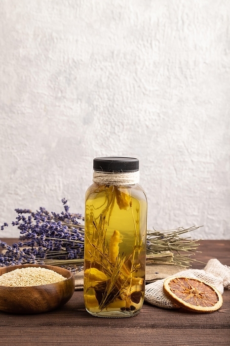 Sunflower oil in a glass jar with various herbs and spices, lavender, sesame, rosemary on a brown wooden background. Side view, copy space, by ULADZIMIR ZGURSKI