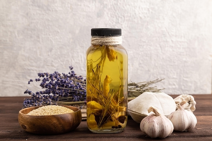 Sunflower oil in a glass jar with various herbs and spices, lavender, sesame, rosemary on a brown wooden background. Side view, copy space, by ULADZIMIR ZGURSKI