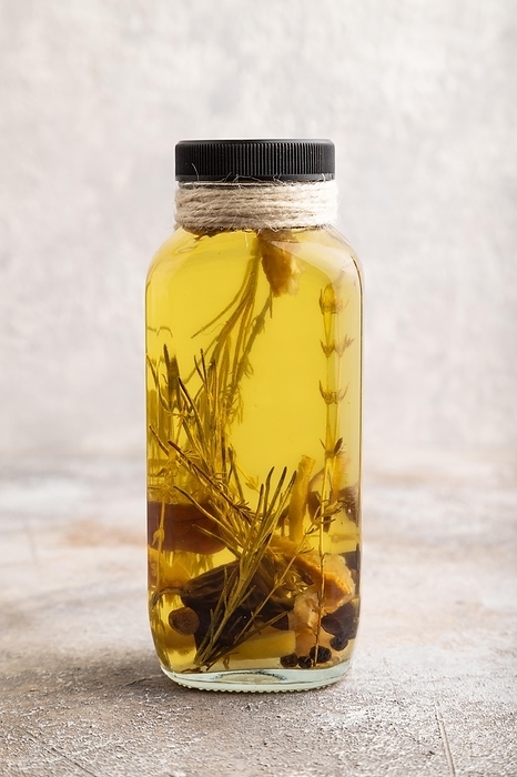 Sunflower oil in a glass jar with various herbs and spices, lavender, sesame, rosemary on a brown concrete background. Side view, close up, by ULADZIMIR ZGURSKI