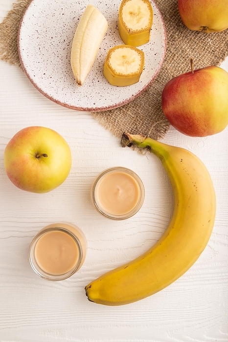 Baby puree with fruits mix, apple, banana infant formula in glass jar on white wooden background. Top view, flat lay, close up, artificial feeding concept, by ULADZIMIR ZGURSKI