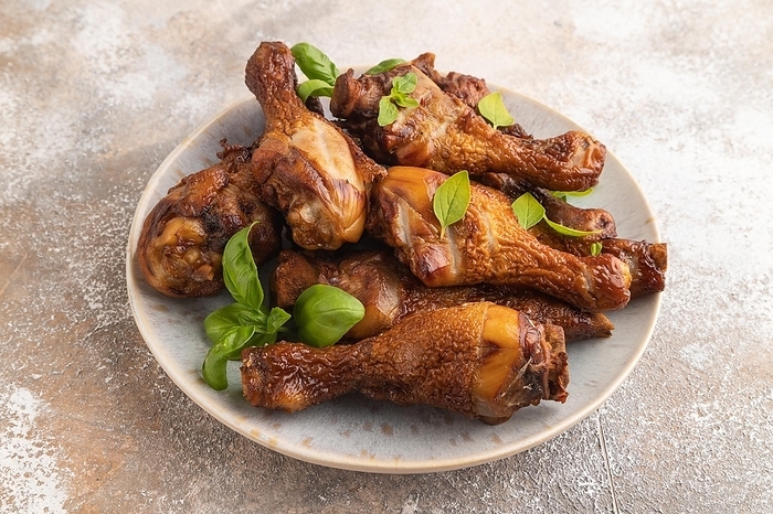 Smoked chicken legs with herbs and spices on a ceramic plate on a brown concrete background. Side view, close up, by ULADZIMIR ZGURSKI