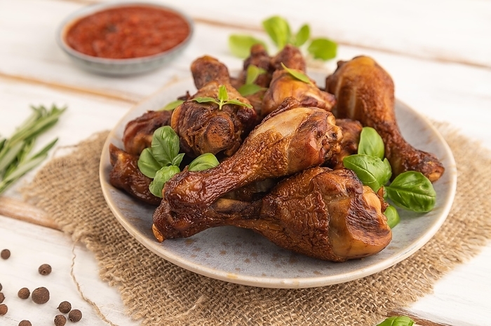 Smoked chicken legs with herbs and spices on a ceramic plate with linen textile on a white wooden background. Side view, close up, selective focus, by ULADZIMIR ZGURSKI