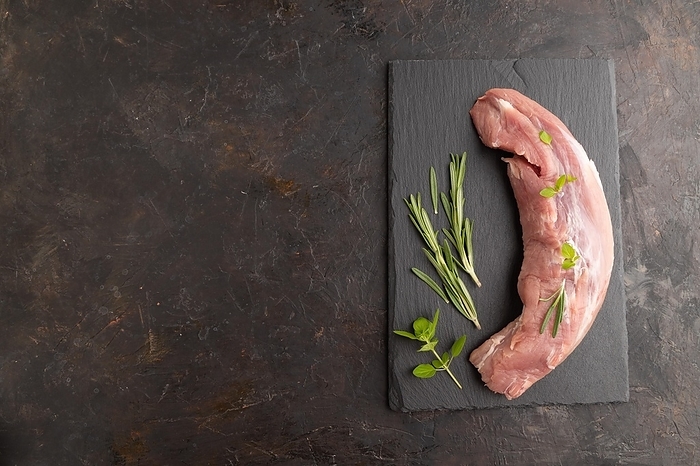 Raw pork meat with herbs and spices on slate cutting board on black concrete background. Top view, flat lay, copy space, by ULADZIMIR ZGURSKI