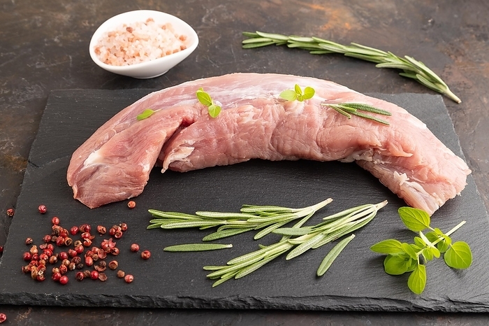 Raw pork meat with herbs and spices on slate cutting board on black concrete background. Side view, close up, by ULADZIMIR ZGURSKI