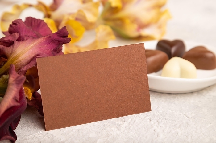 Brown business card with chocolate candies and iris flowers on gray concrete background. side view, copy space, still life. Breakfast, morning, spring concept, by ULADZIMIR ZGURSKI