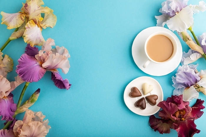 Cup of cioffee with chocolate candies, lilac and purple iris flowers on blue pastel background. top view, flat lay, copy space, still life. Breakfast, morning, spring concept, by ULADZIMIR ZGURSKI
