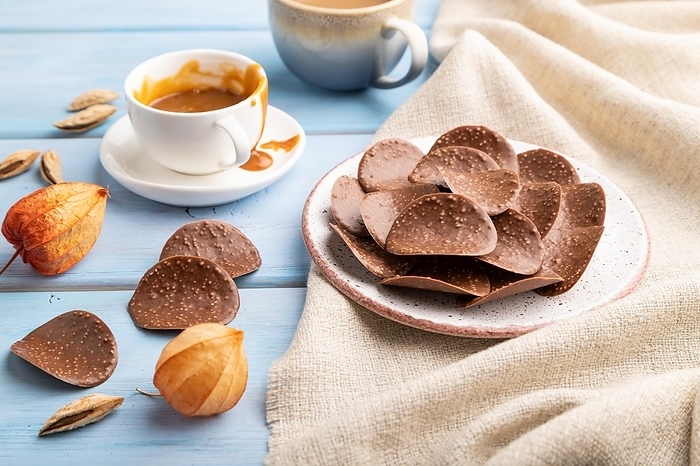 Chocolate chips with cup of coffee and caramel on a blue wooden background and linen textile. side view, close up, by ULADZIMIR ZGURSKI