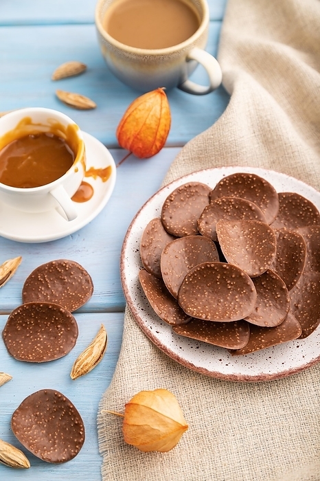 Chocolate chips with cup of coffee and caramel on a blue wooden background and linen textile. side view, close up, selective focus, by ULADZIMIR ZGURSKI