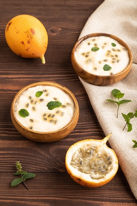 Yoghurt with granadilla and mint in wooden bowl on brown wooden background and linen textile. side view, close up, by ULADZIMIR ZGURSKI