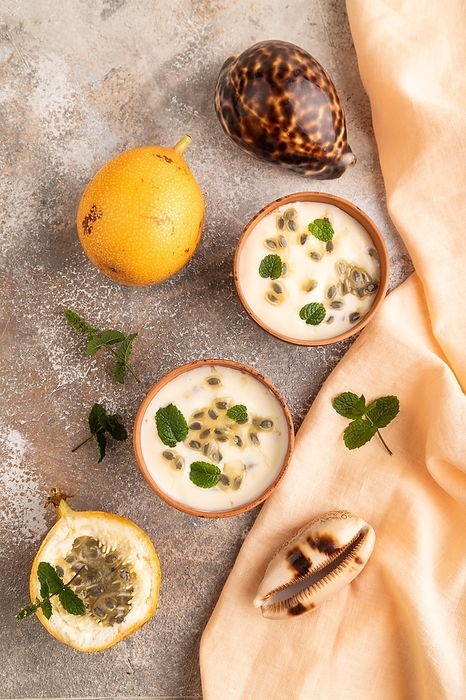 Yoghurt with granadilla and mint in clay bowl on brown concrete background and orange linen textile. top view, flat lay, close up, by ULADZIMIR ZGURSKI