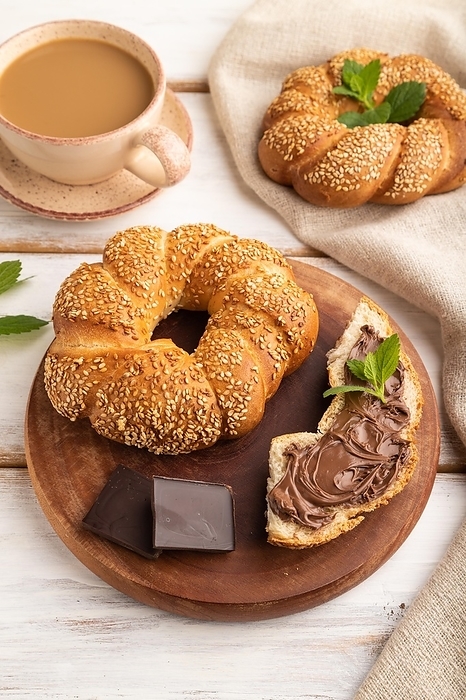 Homemade sweet bun with chocolate cream and cup of coffee on a white wooden background and linen textile. side view, close up, by ULADZIMIR ZGURSKI