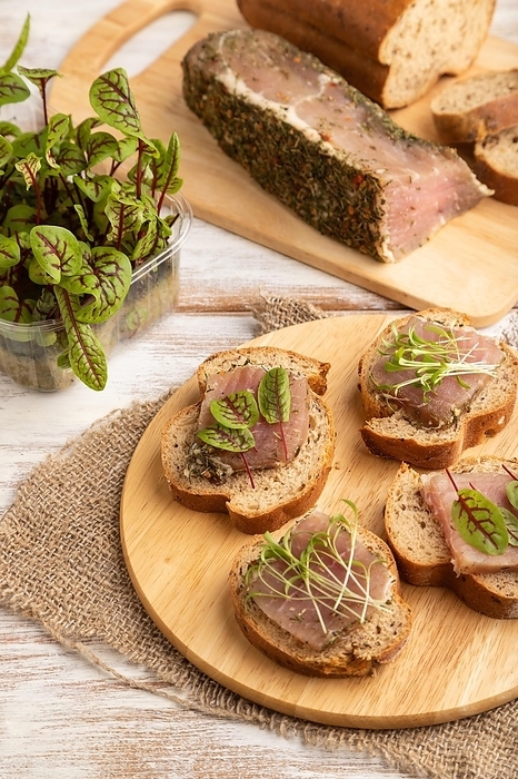 Bread sandwiches with jerky salted meat, sorrel and cilantro microgreen on white wooden background and linen textile. side view, close up, by ULADZIMIR ZGURSKI