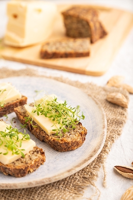 Grain bread sandwiches with cheese and watercress microgreen on gray concrete background and linen textile. side view, close up, selective focus, by ULADZIMIR ZGURSKI