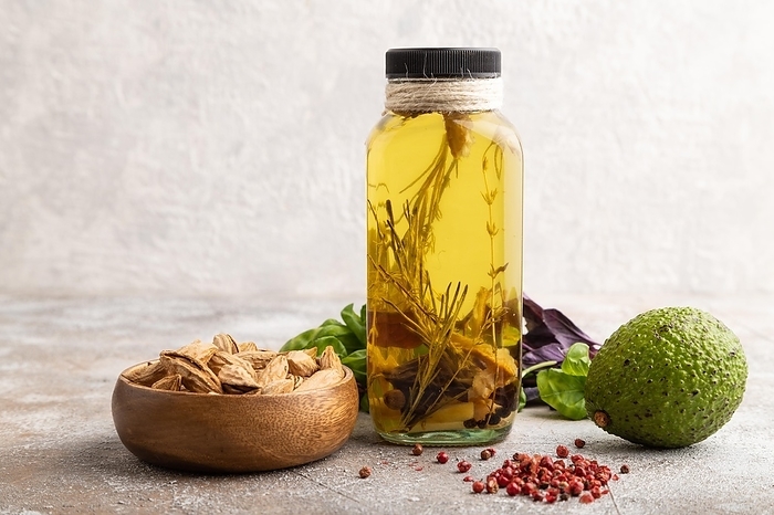 Sunflower oil in a glass jar with various herbs and spices, sesame, rosemary, avocado, basil, almond on a brown concrete background. Side view, copy space, by ULADZIMIR ZGURSKI