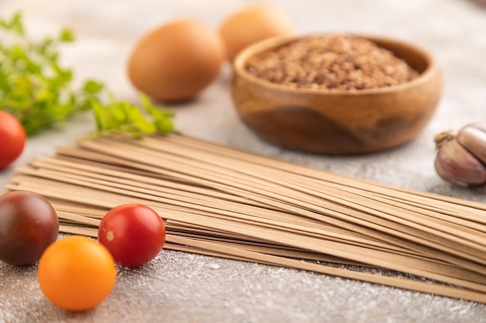 Japanese buckwheat soba noodles with tomato, eggs, spices, herbs on brown concrete background. Side view, close up, selective focus, by ULADZIMIR ZGURSKI