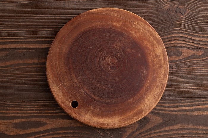 Empty round wooden cutting board on brown wooden background. Top view, flat lay, by ULADZIMIR ZGURSKI