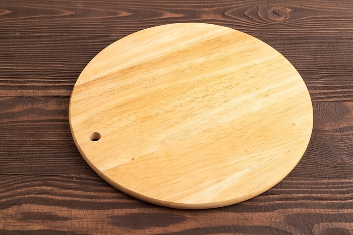 Empty round wooden cutting board on brown wooden background. Side view, close up, by ULADZIMIR ZGURSKI