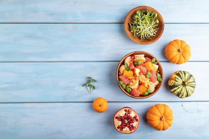 Vegetarian fruit salad of pumpkin, tangerine, pomegranate, grapefruit, sunflower microgreen sprouts on blue wooden background. Top view, flat lay, copy space, by ULADZIMIR ZGURSKI