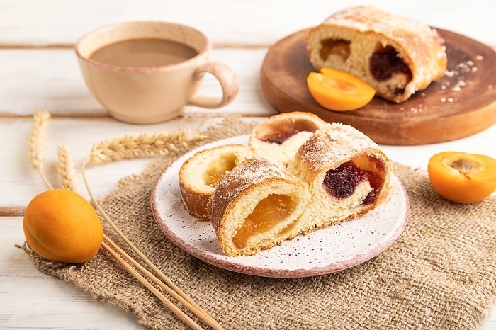 Homemade sweet bun with apricot jam and cup of coffee on white wooden background and linen textile. side view, close up, by ULADZIMIR ZGURSKI