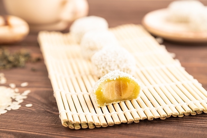 Japanese rice sweet buns mochi filled with pandan and coconut jam and cup of green tea on brown wooden background. side view, close up, selective focus, by ULADZIMIR ZGURSKI