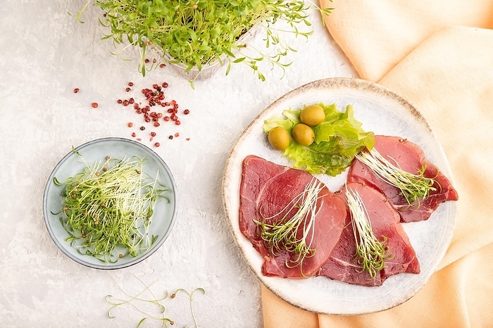 Slices of smoked salted meat with cilantro microgreen on gray concrete background and orange textile. Top view, flat lay, close up, by ULADZIMIR ZGURSKI