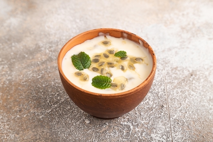 Yoghurt with granadilla and mint in clay bowl on brown concrete background. side view, close up, by ULADZIMIR ZGURSKI