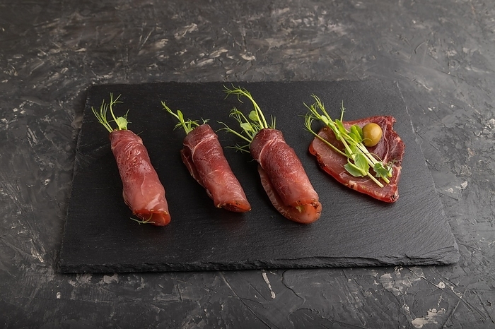 Slices of smoked salted meat with green pea microgreen on black concrete background. Side view, close up, by ULADZIMIR ZGURSKI