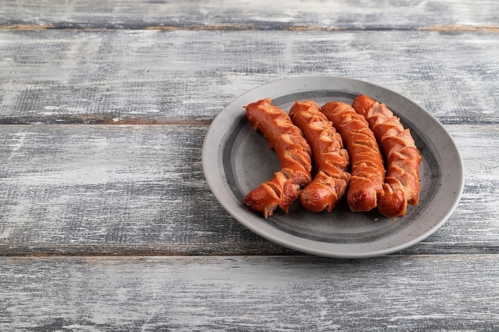 Fried sausage on a gray plate on a gray wooden background. Top view, close up, copy space, by ULADZIMIR ZGURSKI