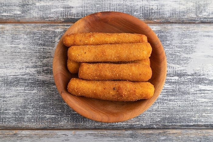 Heap of cheese sticks on a wooden plate on a gray wooden background. Top view, flat lay, close up, by ULADZIMIR ZGURSKI