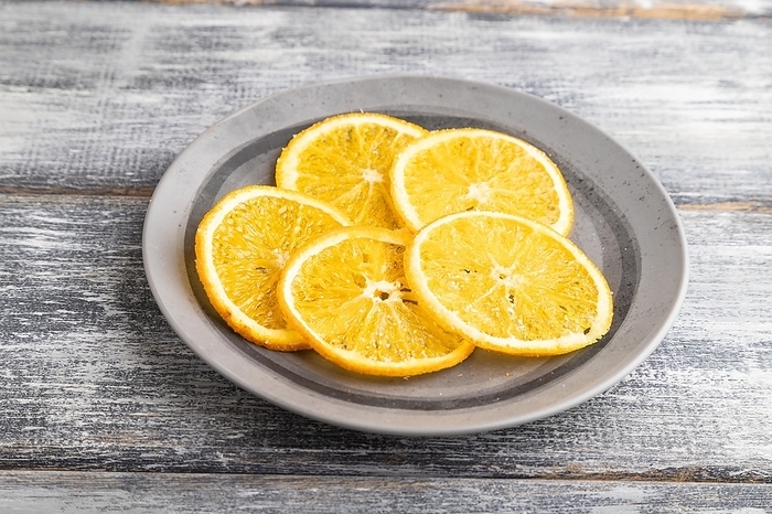 Orange chips on a gray plate on a gray wooden background. Side view, close up, by ULADZIMIR ZGURSKI