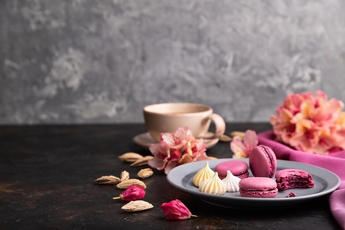 Purple macarons or macaroons cakes with cup of coffee on a black concrete background and pink textile. Side view, copy space, selective focus, by ULADZIMIR ZGURSKI