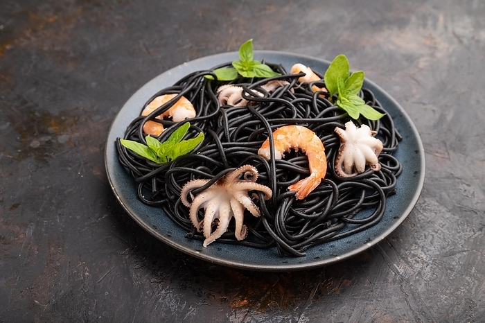 Black cuttlefish ink pasta with shrimps or prawns and small octopuses on black concrete background. Side view, close up, by ULADZIMIR ZGURSKI