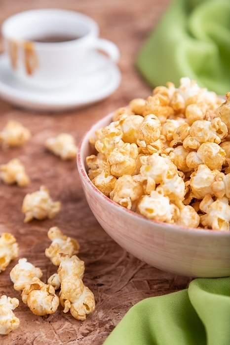 Popcorn with caramel in ceramic bowl on brown concrete background and green textile. Side view, close up, selective focus, by ULADZIMIR ZGURSKI