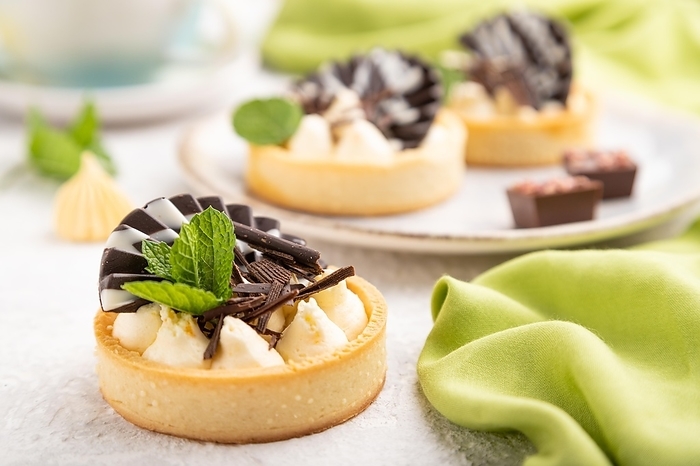Sweet tartlets with chocolate and cheese cream with cup of coffee on a gray concrete background and green textile. Side view, close up, selective focus, by ULADZIMIR ZGURSKI