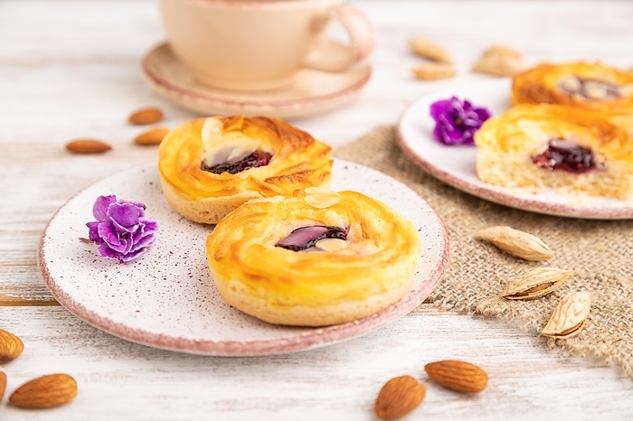 Small cheesecakes with jam and almonds with cup of coffee on a white wooden background and linen textile. Side view, close up, selective focus, by ULADZIMIR ZGURSKI
