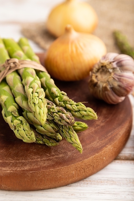 Bunch of fresh green asparagus, garlic, onion on white wooden background. Side view, selective focus. harvest, healthy, vegan food, concept, by ULADZIMIR ZGURSKI