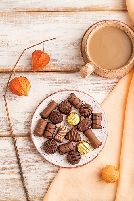 Chocolate candies with cup of coffee and physalis flowers on a white wooden background and orange textile. top view, flat lay, close up, by ULADZIMIR ZGURSKI
