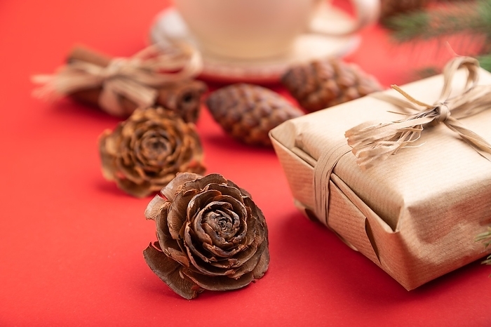 Christmas or New Year composition. Decorations, box, cinnamon, cones, fir and spruce branches, cup of coffee, on a red paper background. Side view, close up, selective focus, by ULADZIMIR ZGURSKI