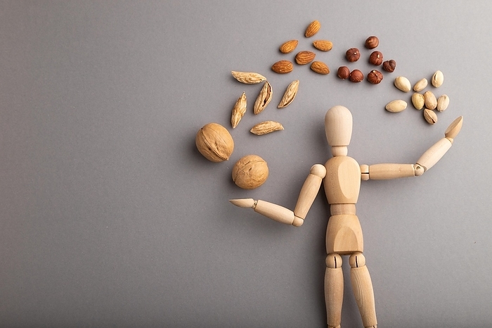Wooden mannequin juggling nuts on gray pastel background. close up, isolated, delivery concept, copy space, by ULADZIMIR ZGURSKI