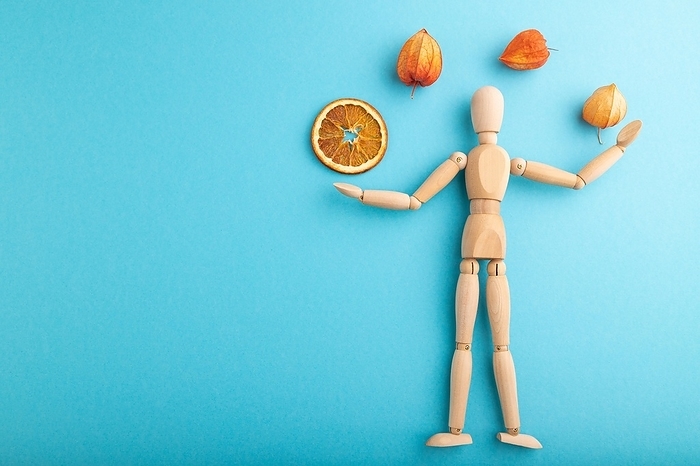Wooden mannequin juggling dried citrus and physalis on blue pastel background. copy space, isolated, by ULADZIMIR ZGURSKI