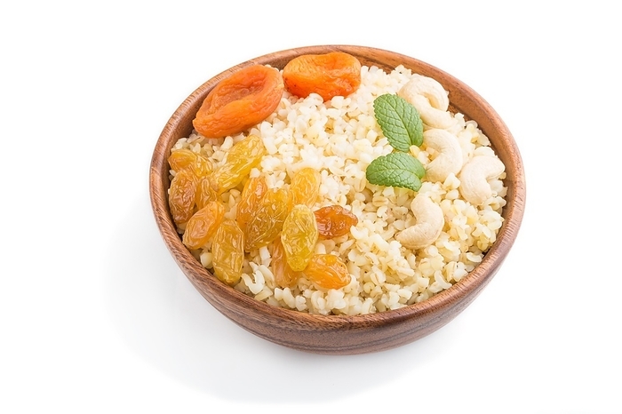 Bulgur porridge with dried apricots, raisins and cashew in wooden bowl isolated on white background. Side view, close up. Turkish traditional cuisine, by ULADZIMIR ZGURSKI