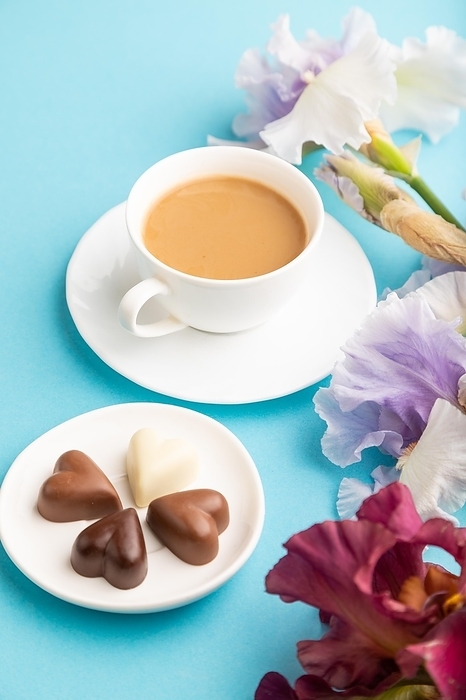 Cup of cioffee with chocolate candies, lilac and purple iris flowers on blue pastel background. side view, copy space, still life. Breakfast, morning, spring concept, by ULADZIMIR ZGURSKI