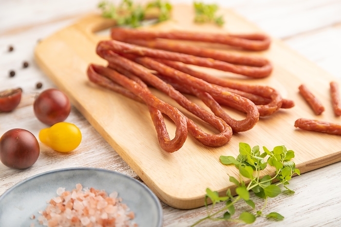 Traditional polish smoked pork sausage kabanos on cutting board with salt and pepper on white wooden background. Side view, close up, selective focus, by ULADZIMIR ZGURSKI