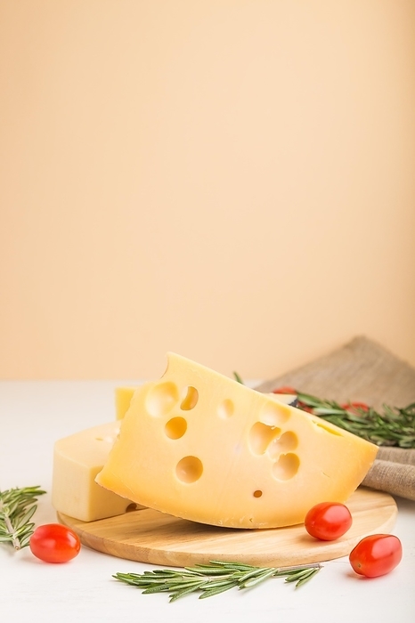 Various types of cheese with rosemary and tomatoes on wooden board on a white and orange background and linen textile. Side view, close up, copy space, selective focus, by ULADZIMIR ZGURSKI